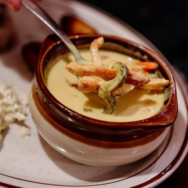 A spoon lifts chicken and vegetables from a creamy Mexican soup in a brown and white bowl.