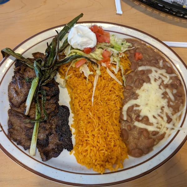 Grilled steak with green onions, orange rice, refried beans with cheese, and a side salad with sour cream.