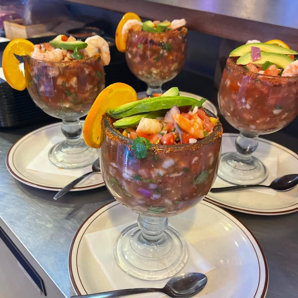 Four shrimp cocktails, garnished with orange slices and avocado, on a metal counter at Jacky's Restaurant.