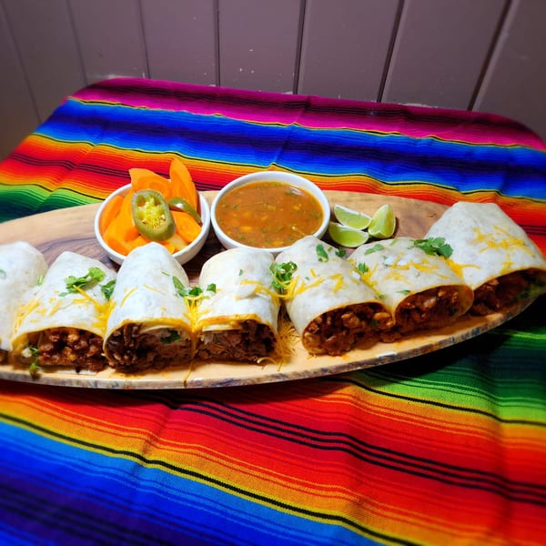 Jacky's Restaurant burritos with salsa, pickled carrots, jalapeños, and lime on a colorful Mexican blanket.