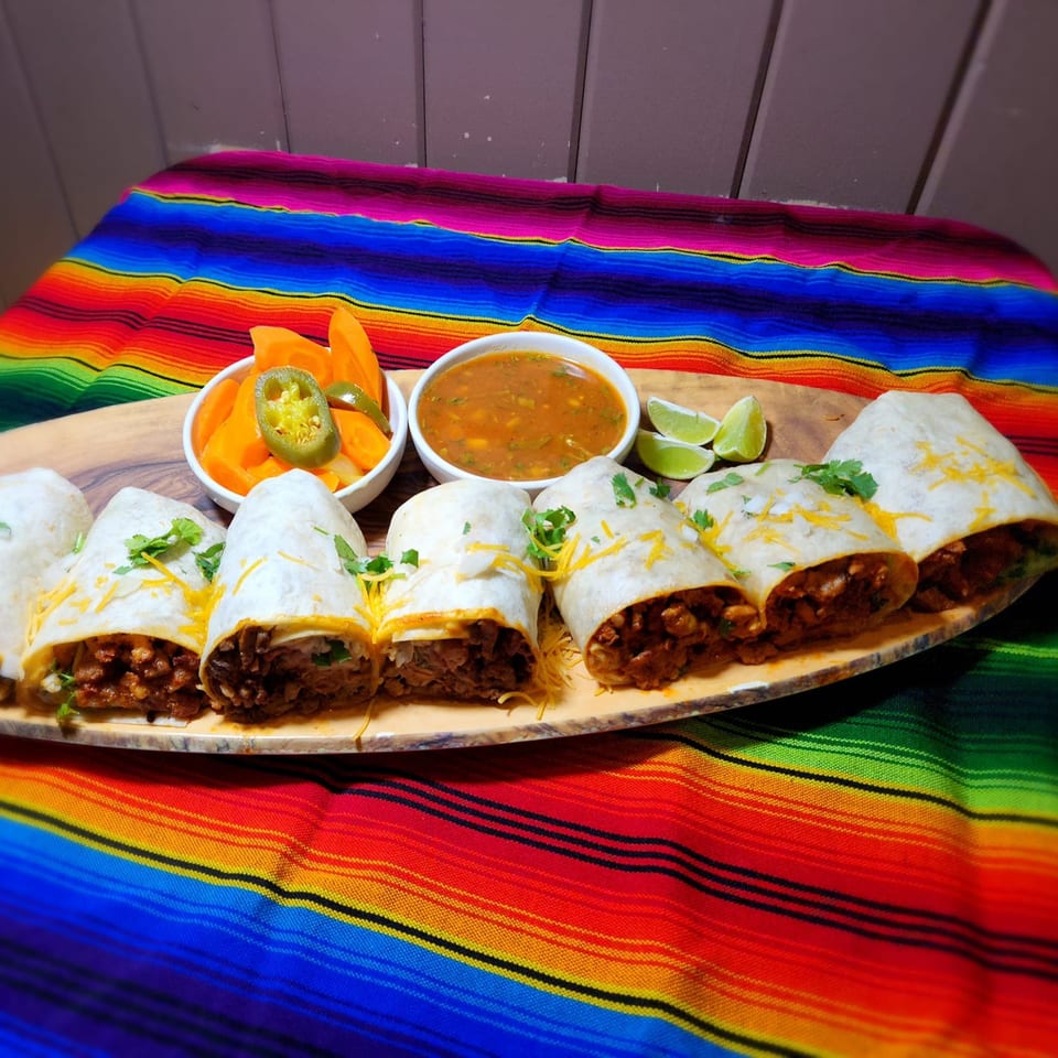 Jacky's Restaurant burritos with salsa, pickled carrots, jalapeños, and lime on a colorful Mexican blanket.