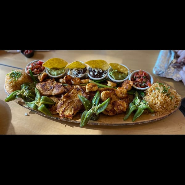 A large Mexican platter with grilled chicken, shrimp, rice, peppers, guacamole, salsa, and black beans.
